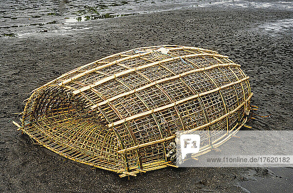 A traditional woven bamboo fishing trap on a volcanic black sand beach; Manado  North Sulawesi  Indonesia