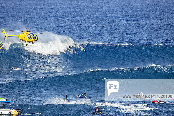 A helicopter filming a tow-in surfer at Peahi (Jaws) off Maui,  Hawaii. This was a medium day at the famous surf spot; Peahi,  Maui,  Hawaii,  United States of America
