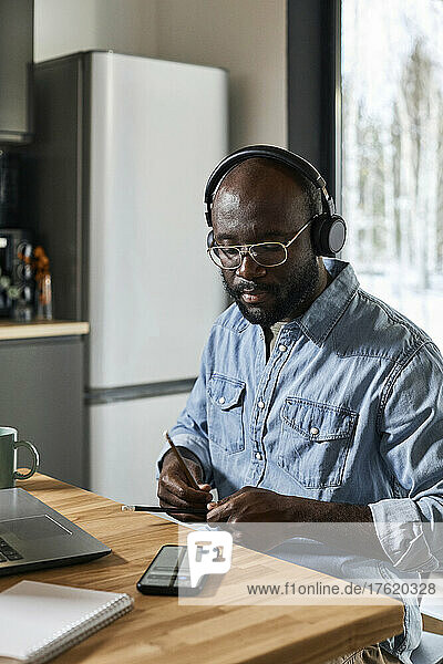 Man with headphones playing rhythm using pencils on dining table at home