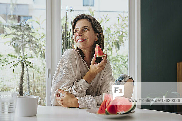 Happy woman holding watermelon slice sitting at home