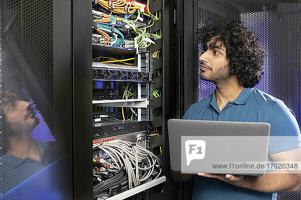 IT support holding laptop checking network server in industry