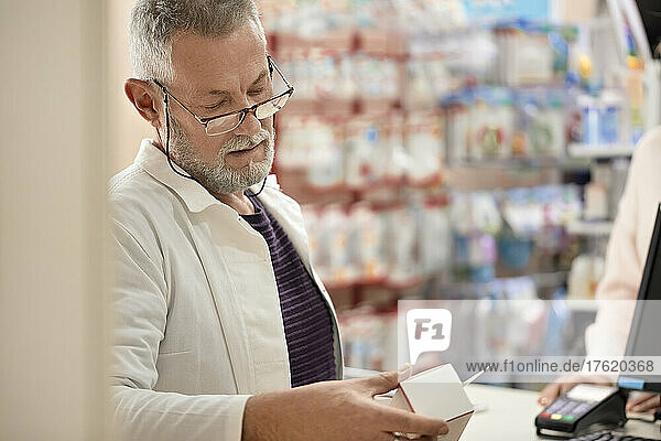 Pharmacist reading instructions on medicine box at pharmacy store