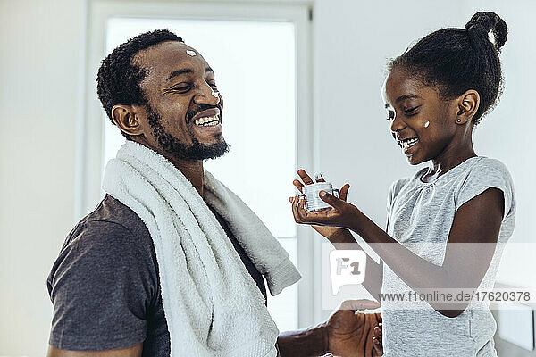 Smiling daughter applying moisturizer to father in bathroom