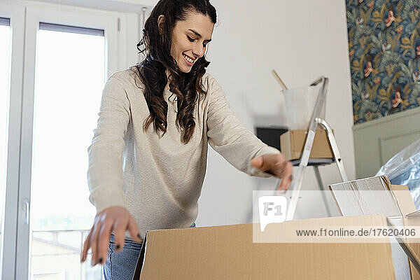 Smiling woman unpacking carboard boxes moving into new home