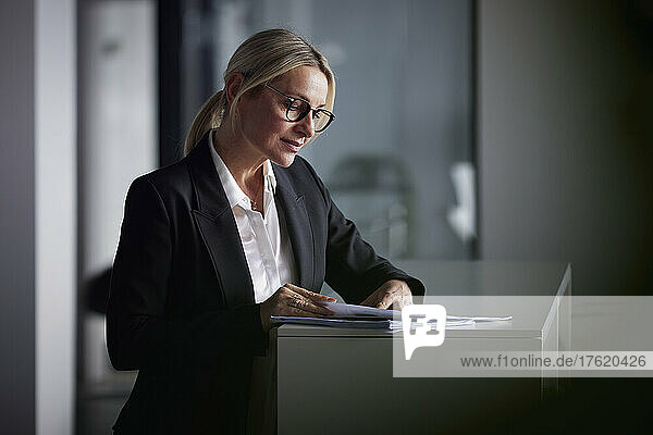 Businesswoman reading documents standing at desk in office