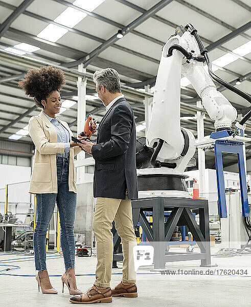 Technician showing model of robotic arm discussing with businessman in factory