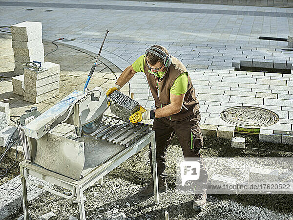 Construction worker holding paving stone by machinery for cutting at site