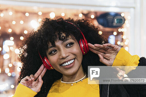 Beautiful happy woman enjoying music through wireless headphones at night