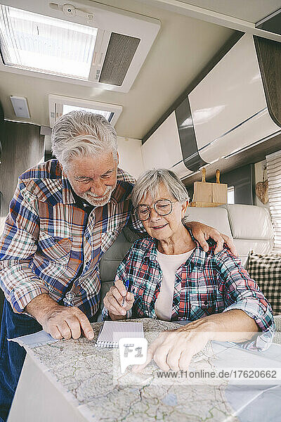 Lächelndes älteres Paar diskutiert im Wohnmobil über Reiseführerkarte