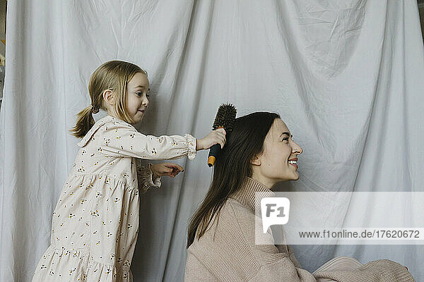 Cute blond girl combing mother's hair at home