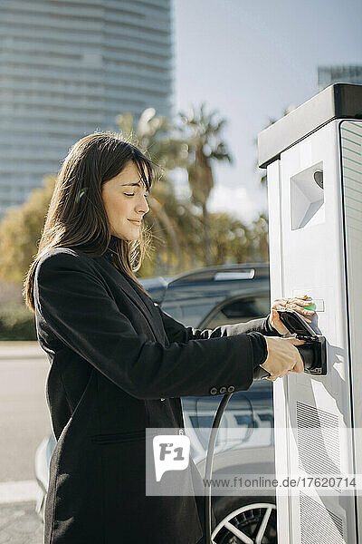 Smiling woman charging electric car at charging station