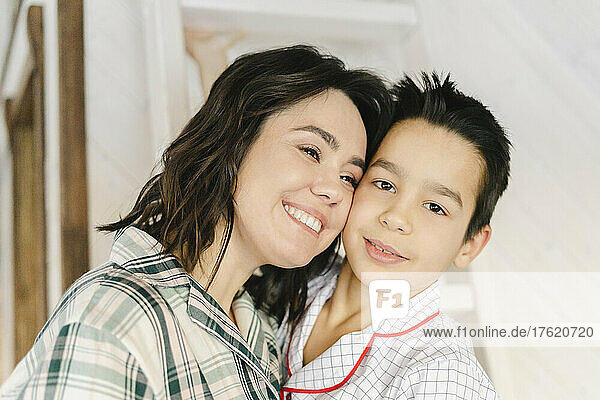 Smiling mother with son standing cheek to cheek at home