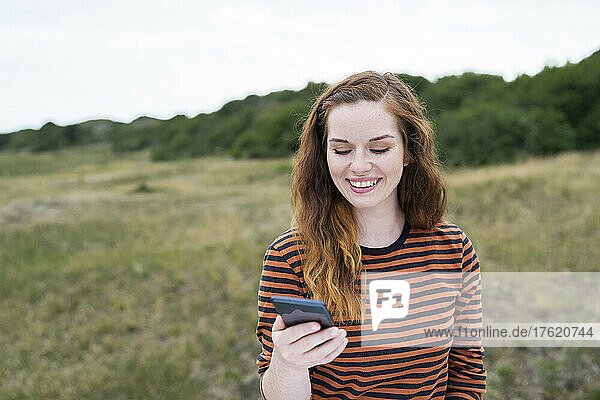 Lächelnde rothaarige Frau benutzt Smartphone auf der Wiese