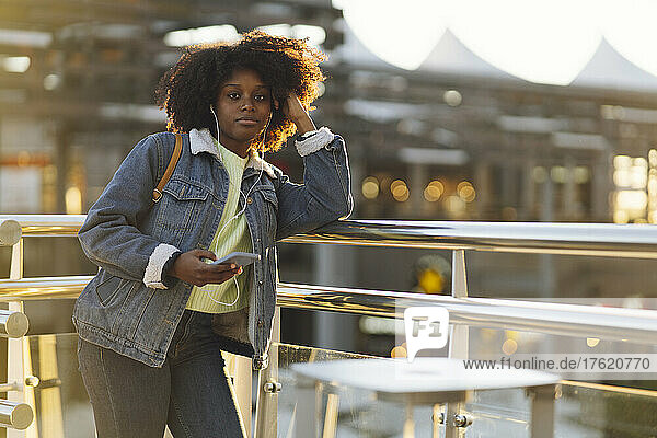Frau mit Smartphone lehnt bei Sonnenuntergang am Geländer