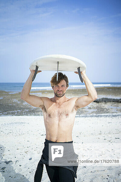 Shirtless carrying surfboard on sunny day at beach