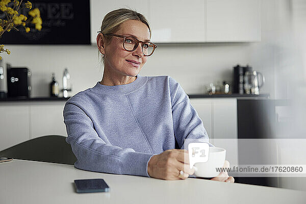 Businesswoman wearing eyeglasses holding coffee cup sitting at table