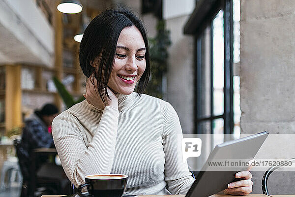 Smiling woman holding tablet PC sitting at cafe
