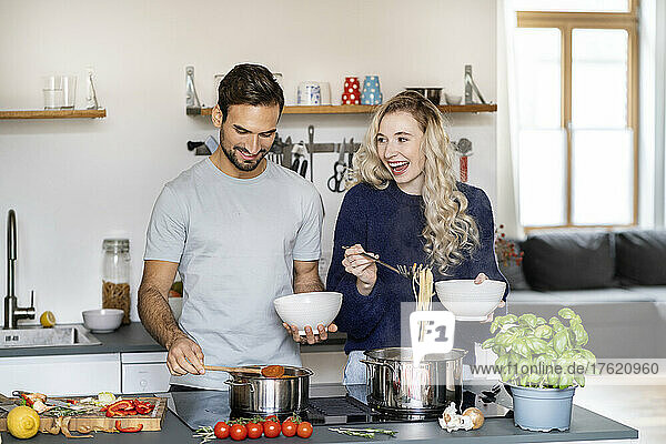 Happy woman serving spaghetti standing by boyfriend in kitchen