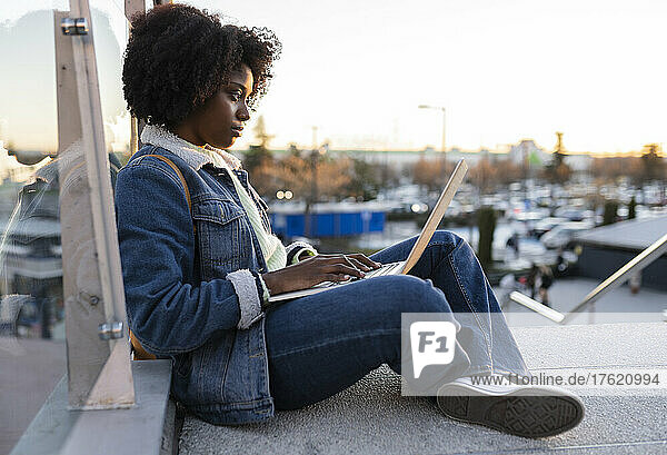Young woman using laptop sitting on staircase at sunset