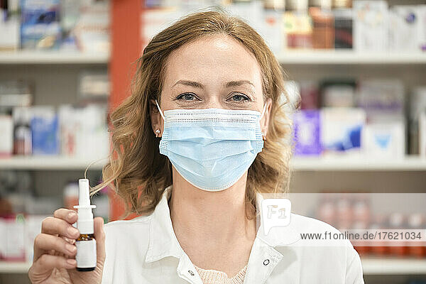 Apothekerin trägt eine schützende Gesichtsmaske und hält eine Flasche Nasenspray in der Apotheke