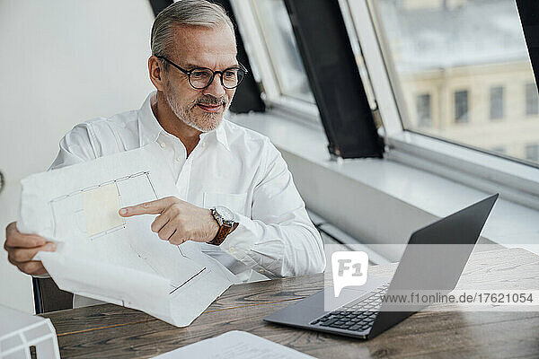 Architect with document on video call over laptop at work place