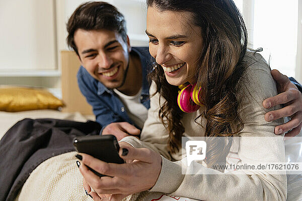 Happy woman sharing smart phone with boyfriend in bedroom