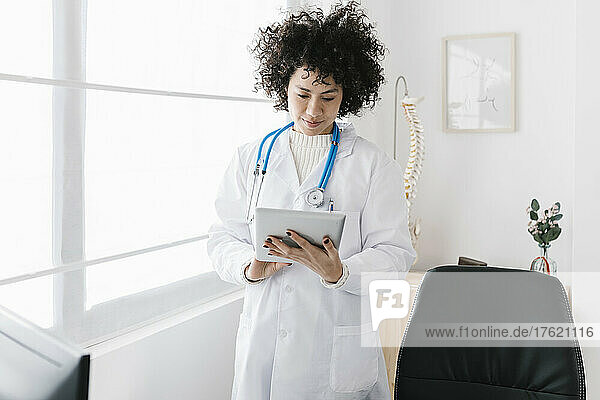 Doctor using tablet PC standing by window at medical clinic