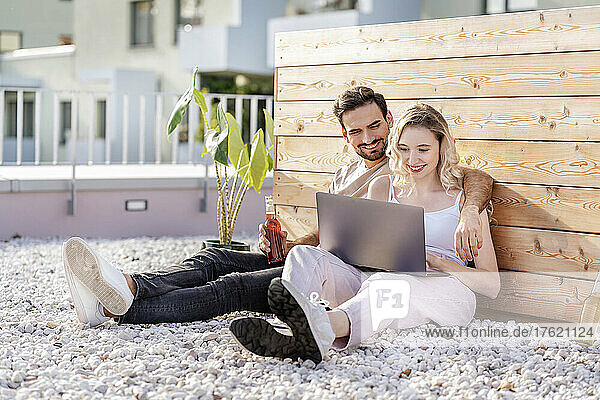 Smiling young couple sharing laptop on sunny day