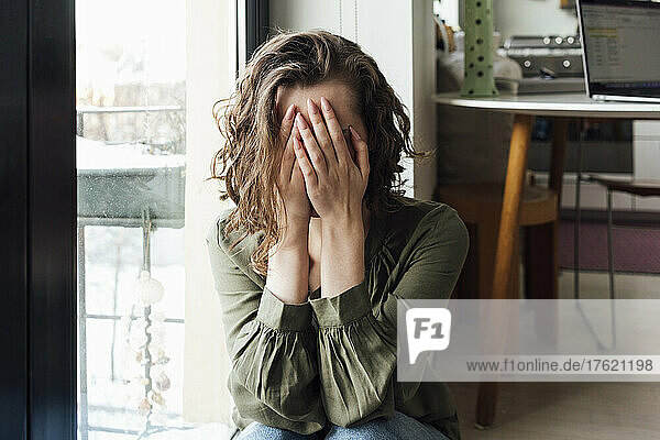 Depressed woman covering face with hands at home