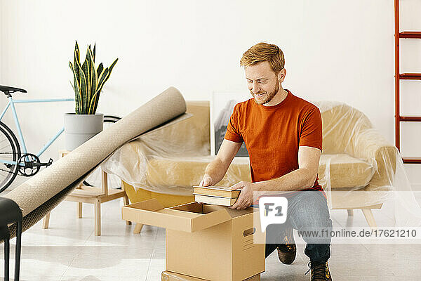 Young man removing books from box in living room at home