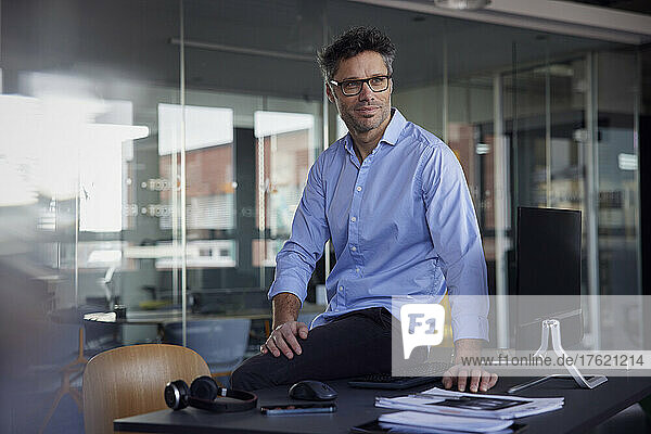 Businessman wearing eyeglasses sitting on desk in office