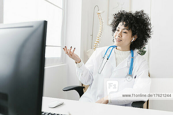 Doctor wearing in-ear headphones discussing on video call at medical clinic