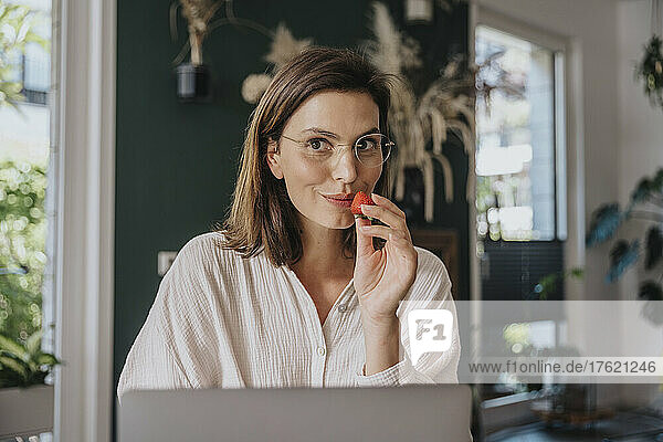 Working woman with eyeglasses holding strawberry at home office