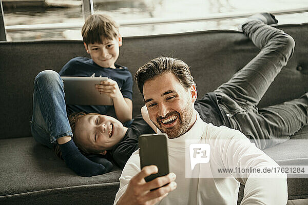 Cheerful father with sons taking selfie through mobile phone at home