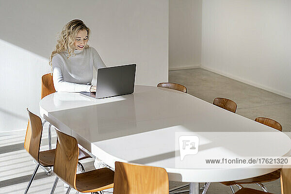 Smiling young woman using laptop sitting at table