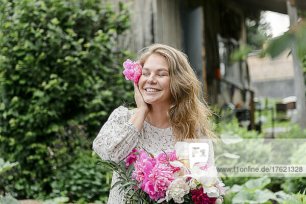 Glückliche blonde Frau mit geschlossenen Augen und rosa Blume im Garten