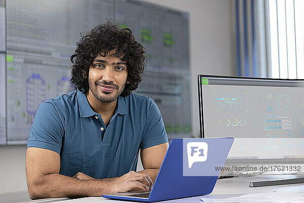 Smiling technician with laptop at desk in control room