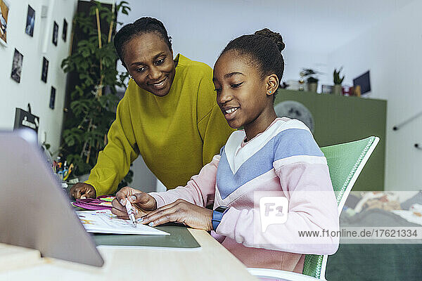 Mutter blickt Tochter beim Lernen am Tablet-PC im Schlafzimmer an