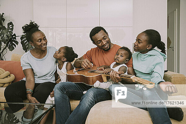 Smiling father playing guitar by family in living room