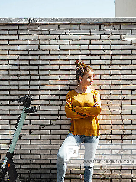 Young woman with arms crossed by electric push scooter