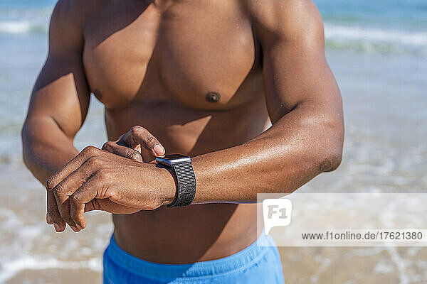Shirtless man touching smart watch on sunny day