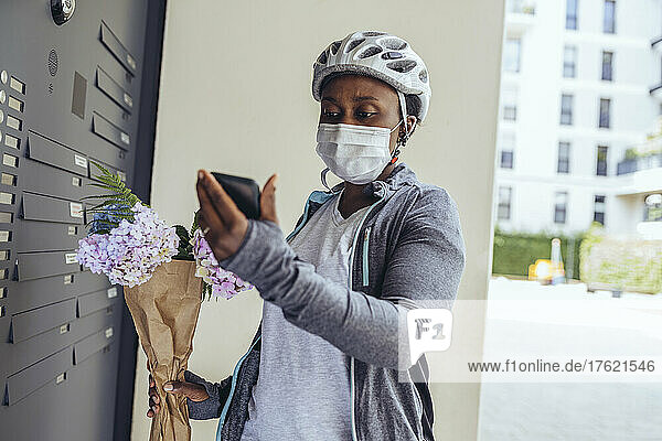 Delivery woman with protective face mask holding bouquet at entrance door