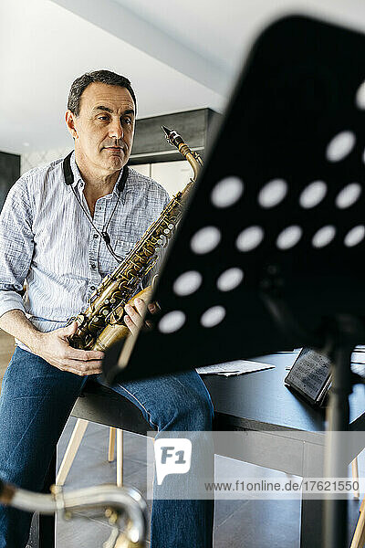 Saxophonist with saxophone sitting on table at home
