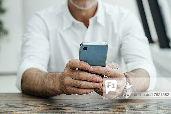 Businessman text messaging on smart phone at desk in office