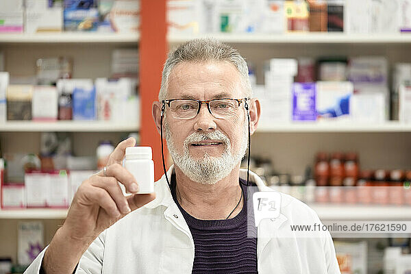 Pharmacist wearing eyeglasses holding bottle of medicine at pharmacy store