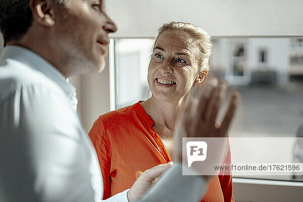 Businessman talking with smiling businesswoman standing in office