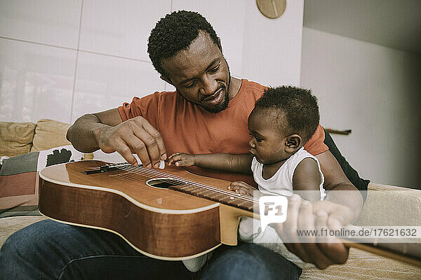 Father showing guitar to baby boy in living room