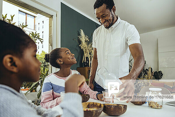 Smiling father pouring milk for daughter at table