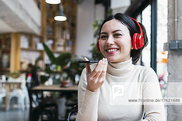 Happy woman wearing wireless headphones talking on mobile phone through speaker at cafe