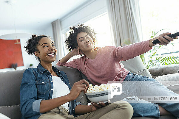 Happy women watching TV sitting on sofa in living room at home